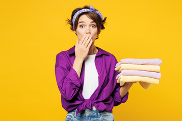 Young shocked excited surprised woman wears purple shirt do housework tidy up hold pile of towels...
