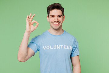 Young happy man wears blue t-shirt white title volunteer look camera showing okay ok gesture...