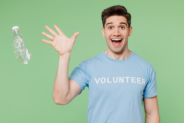 Young man wears blue t-shirt white title volunteer throw away plastic pet bottle isolated on plain pastel green background. Voluntary free work assistance help ecology problem charity grace concept.