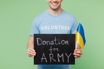 Close up young man wear blue t-shirt title volunteer hold card sign with donation for army title text Ukrainian flag isolated on plain pastel green background Voluntary free work help charity concept