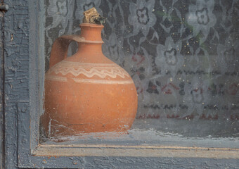 Cay jug in the wooden window of an old traditional house. Old style pottery used as decoration for...
