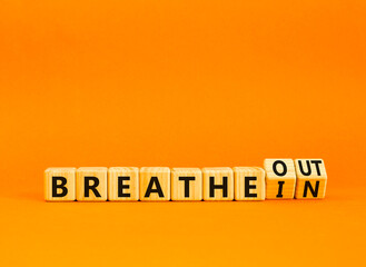 Breathe in and out symbol. Concept words Breathe in to Breathe out on beautiful wooden cubes. Beautiful orange table orange background. Medical, lifestyle and breathe in and out concept. Copy space.