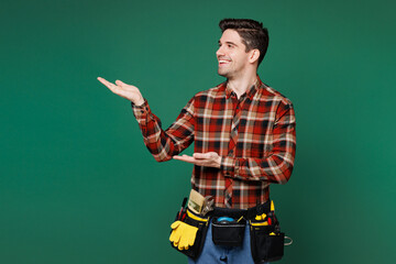 Young employee laborer handyman man wear red shirt point hands arms finger aside on area isolated on plain green background. Instruments accessories for renovation apartment room. Repair home concept.