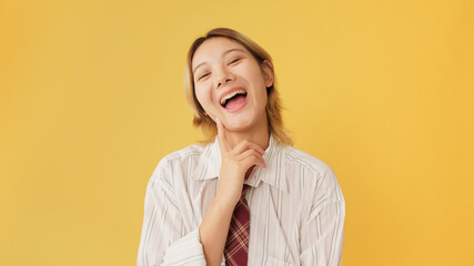 Smiling young woman dressed in shirt and tie looking at camera isolated on yellow background in studio