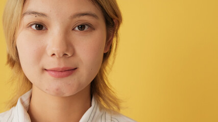 Portrait of young woman looking at camera, isolated on yellow background in studio