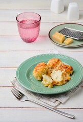 Cooked cauliflower grantin with bechamel sauce and cheese on a green ceramic plate on a light wooden background. Vegetarian recipes; side dishes.