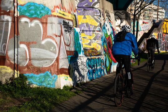 Charenton-le-Pont, France - January 10, 2021: Urban art and healthy lifestyle in Parisian suburbs. Graffiti on the bridge over Marne river and cycling people. Val-de-Marne, Ile-de-France, France.