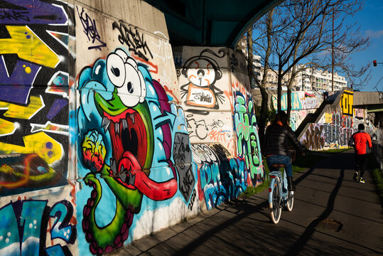 Charenton-le-Pont, France - January 10, 2021: Urban art and healthy lifestyle in Parisian suburbs. Graffiti on the bridge over Marne river; cycling and jogging  people. Val-de-Marne, Ile-de-France.