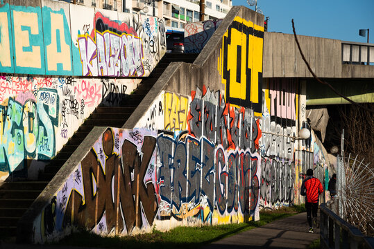 Charenton-le-Pont, France - January 10, 2021: Urban art and healthy lifestyle in Parisian suburbs. Graffiti on bridge over Marne river and jogging man. Val-de-Marne, Ile-de-France, France.
