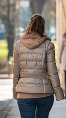 Rear view of trendy young woman in brown jacket and jeans walking on city street in spring. Female fashion concept. Back view. Trendy casual outfit. Street style
