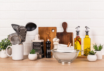 A variety of wooden and metal kitchen utensils on a wooden countertop. Glass bottles with oil in a...