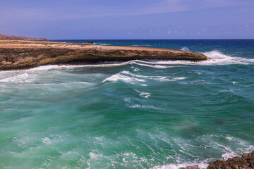 Scenic vista of Caribbean Sea waves breaking against the rocky coastline of Aruba.