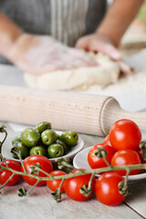Cherry tomatoes closely on the table in the background person kneading the dough with his hands.
