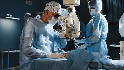 A surgeon looks through a microscope in the operating room. A doctor uses a microscope during eye...