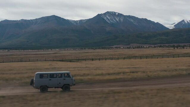 Aerial side view suv car minibus speed driving dirt dust mountain road in steppes. Picturesque snowy caps in wild nature. Road car trip, adventure travel tourism vacations