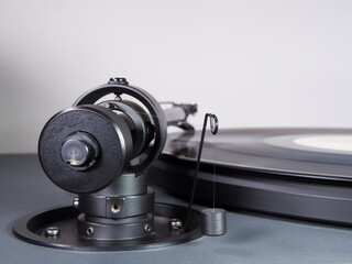 Closeup of the rear of a tonearm with a suspended balancing weight. The stylus / needle is playing a vinyl LP record on a turntable.