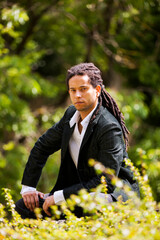 Brazilian individual with stylish rastas, dressed in a suit while strolling in a park