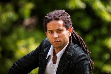 Brazilian individual with stylish rastas, dressed in a suit while strolling in a park