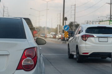 Rear side view of white car with tail lights. Environment of car in the day time. Rush hour in the...