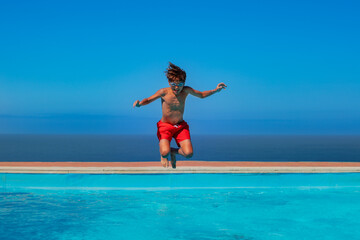 Cute tanned teen in goggles jump carefree at a seaside pool