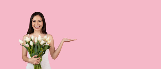 Joyful young woman with tulips presenting copy space with hand on pink, panorama