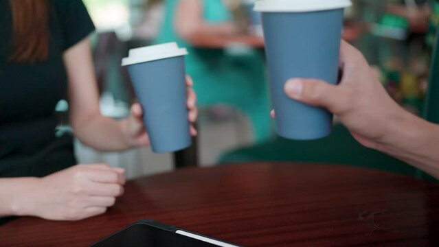 Close-up of a woman and man clinking coffee cups to celebrate success in their business.