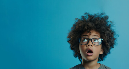 boy adorned with glasses and voluminous hair, set against a striking blue background. His wide-eyed expression adds intrigue and captivation to the scene. space for copy for various creative endeavors