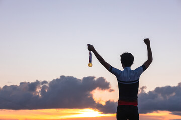 Fototapeta na wymiar Silhouette of an athlete celebrating the gold medal against a sunset sky adorned with golden clouds in the background. Ideal for conveying the spirit of success in sporting events