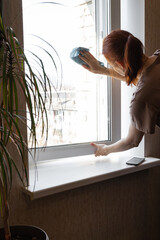 Young Smiling Woman Washing Window with Sponge. Happy Beautiful Girl wearing Protective Gloves...