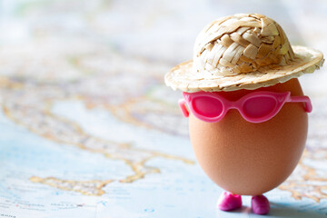 Easter egg with sunglasses in hat on map, creative easter travel concept