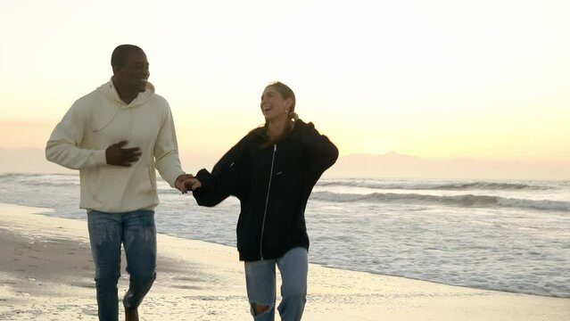 Casually dressed loving young couple running hand in hand along through waves on shoreline watching beautiful sunrise morning over beach and sea in South Africa - shot in slow motion