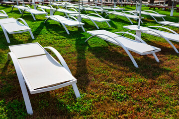 White deck chairs on the green grass at the hotel. Sun loungers on the lawn