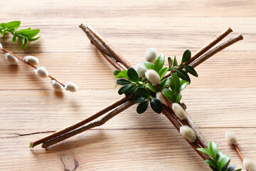 Cross made of branches decorated with boxwood twigs and catkins on wooden background. Creative easter religious concept