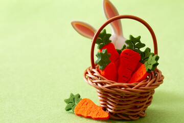 Basket with cute carrots and bunny ears on green background, easter decoration concept 