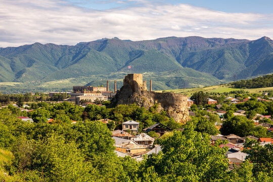 Surami fortress in Georgia, ruins of medieval castle at the top of a hill with Georgian national flag on top, rural architecture around, Likhi Mountain Range in the background.