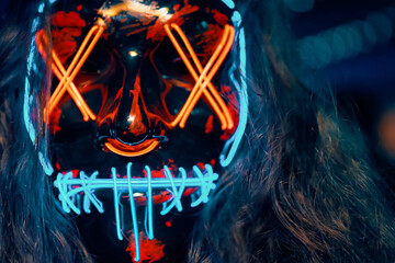 Close up of person with long disheveled hair in a lighting neon glowing mask. Halloween dress-up...