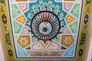 Kutaisi Synagogue inside view of richly decorated ceiling with colorful geometric and floral pattern paintings and chandelier.
