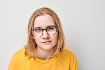 Portrait of young individual with glasses against neutral background expressing thoughtful demeanor