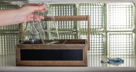 Reuse and return, eco image. Empty Glass milk bottles placed into a crate, on a kitchen windowsill ready for collection by the milkman. Foil bottle tops pilled up for recycling. 
