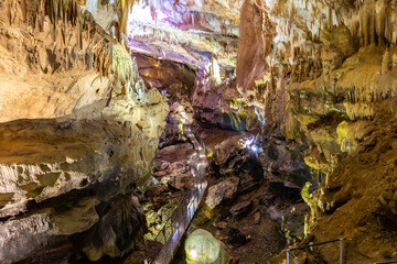 Prometheus Cave Natural Monument landscape, Georgia, main hall view with tourist walking platforms, hanging stone curtains, stalactites and stalagmites, colorful illuminated rock formations.