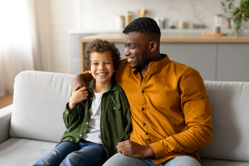 Fototapeta premium Happy black boy and dad sitting on couch at home