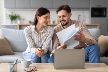 Smiling european spouses reviewing documents in front of laptop