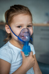 smiling little girl are sitting and holding a nebulizer mask leaning against the face, airway...