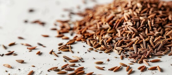 A close-up view of a pile of caraway seeds neatly arranged on top of a white table. The seeds are small, oval-shaped, and brown in color. They appear to be sitting undisturbed on the smooth surface. - obrazy, fototapety, plakaty
