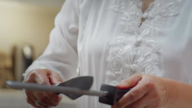Closeup shot of an Asian woman sharpening a knife