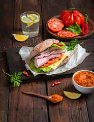 Sandwich with pulled ham, green salad and tomatoes on dark wooden background