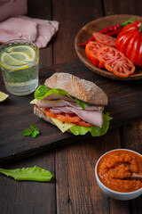 Sandwich with pulled ham, green salad and tomatoes on dark wooden background