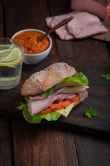 Sandwich with pulled ham, green salad and tomatoes on dark wooden background