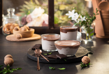 Chocolate and cream dessert in glass bowls against the background of a window with flowers