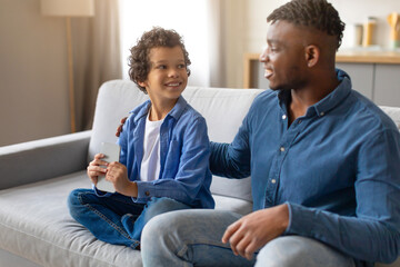 Smiling black preteen boy with phone looking at attentive father